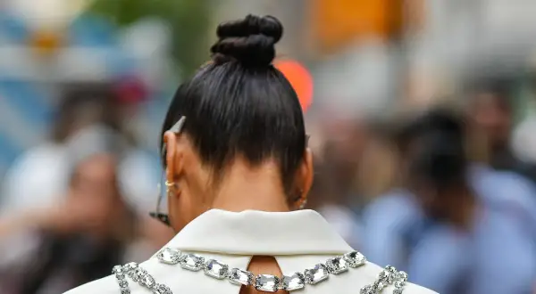 Capelli raccolti in un elegante chignon alto, impreziositi da una collana scintillante su un abito bianco.