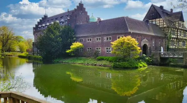 Schloss Wittringen, ein imposantes Backsteingebäude, spiegelt sich im Wasser eines umliegenden Grabens.
