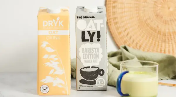 Dwa kartony mleka roślinnego (DRYK i Oatly) oraz szklanka zielonego napoju.