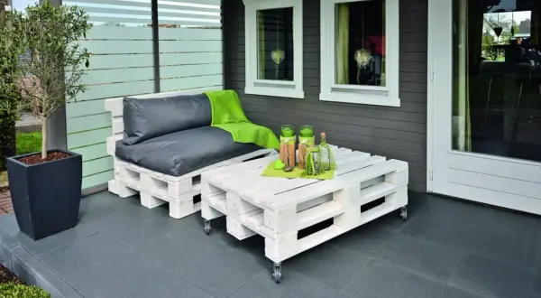 Sofá y mesa de centro hechos con pintura para palets, con cojines grises y manta verde.