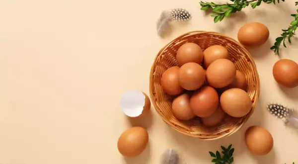 Koszyk pełen jajek, piórka i gałązki zieleni. Widać też skorupkę po jajku. Makro zbliżenie na naturalne piękno.