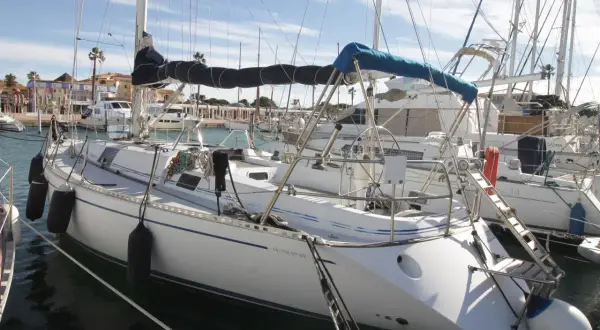 Barche a vela ormeggiate in un porto, con la scritta "Genesi Sport" su una di esse. Cielo azzurro con nuvole.