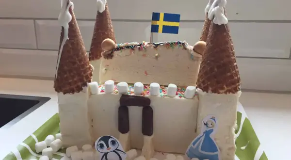 En fantasifull glasstårta formad som ett slott, perfekt för barn. Med svenska flaggan på toppen och dekorerad med marshmallows, strössel och söta figurer.
