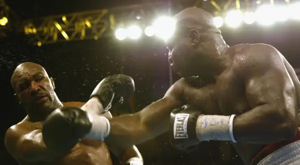 Two boxers clash under bright lights. The sound of their punches echoes, a testament to the force behind each blow.