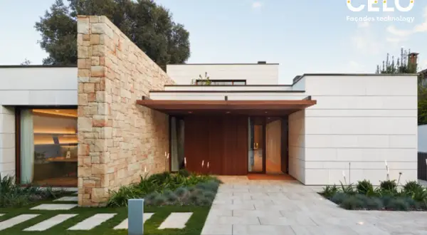 Casa moderna con acabados de fachadas de piedra y paneles blancos. Un camino de baldosas conduce a la entrada principal de madera.