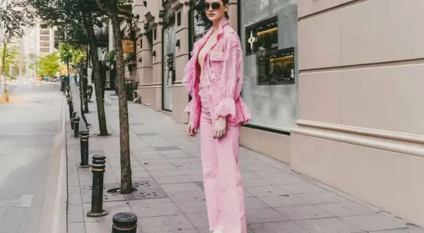 Ein Model präsentiert, wie man **pinke Hose kombinieren** kann: mit einem passenden pinken Spitzen-Blazer und weißen Sneakern.