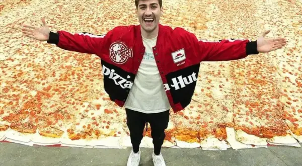 Mężczyzna w kurtce Pizza Hut stoi na gigantycznej pizzy.