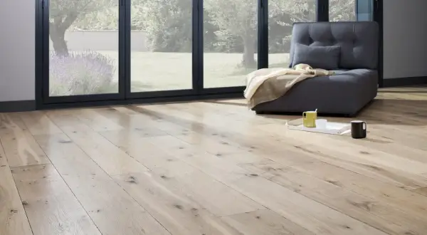 Un salon lumineux avec un parquet clair, une banquette grise et une vue sur un jardin verdoyant. Idéal pour peindre un parquet et créer une ambiance cosy.