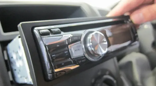 Dłoń wyjmuje radio samochodowe. Może to być pierwszy krok, jak znaleźć kod do radia, jeśli go zapomniałeś.