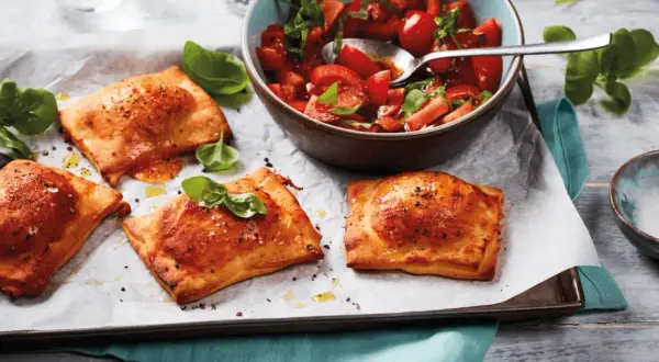 Goldbraune Teigtaschen, gefüllt und gebacken, zeigen, was man aus pizzateig machen kann. Dazu ein frischer Tomatensalat.