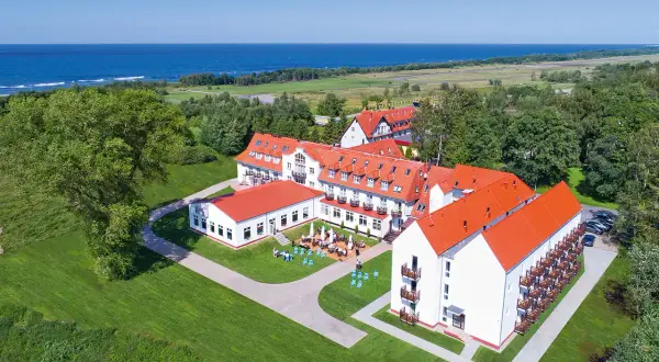Hotel Mona Lisa Kołobrzeg z widokiem na morze. Białe budynki z czerwonymi dachami otoczone zielenią.