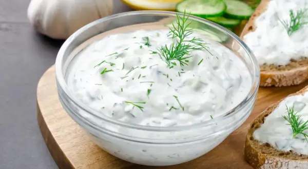 Un bol de salsa de yogur con eneldo y pepino, listo para untar en pan tostado.