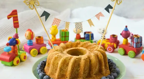 Saftiger Kuchen ohne Zucker für Kinder, dekoriert mit Blaubeeren und bunten Holzspielzeugen. Perfekt für den ersten Geburtstag!
