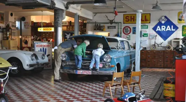 Familie inspiziert blauen Oldtimer in Werkstatt. Die Restaurierung des Autos scheint ein gemeinsames Projekt zu sein.