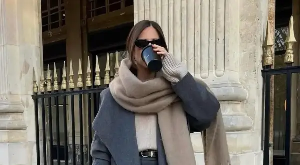 Stilvolle Frau trinkt Kaffee, kombiniert grau und beige mit einem Oversize-Schal und Mantel.