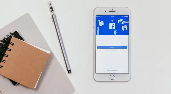 Telefon z ekranem logowania Facebooka. Obok notatnik i długopis. Jak sprawdzić hasło na FB będąc zalogowanym?