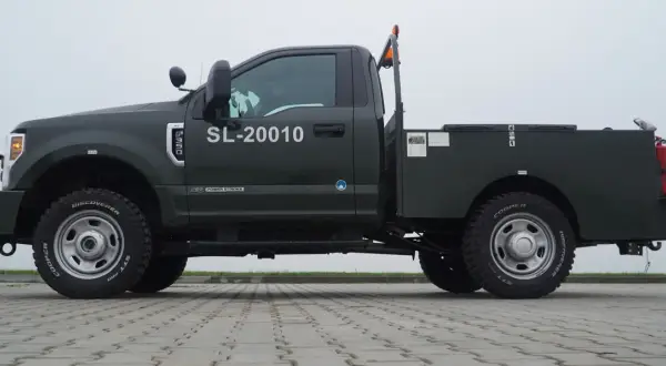 Ciemnozielony Ford F350 z platformą, numerem SL-20010 i pomarańczowym kogutem na dachu.
