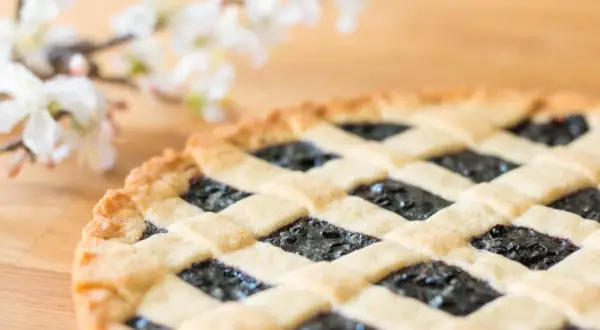 Ein köstliches Crostata-Rezept mit Blaubeerfüllung und Gittermuster, daneben zarte weiße Blüten.