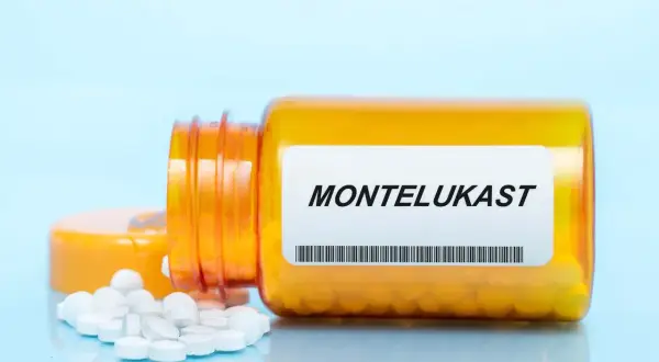 Pomarańczowa butelka leku z etykietą MONTELUKAST, z której wysypały się białe tabletki.