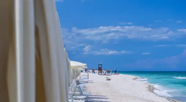File di ombrelloni bianchi aprono la vista sulla spiaggia di Marotta, con lettini pronti e il mare turchese sotto un cielo azzurro.