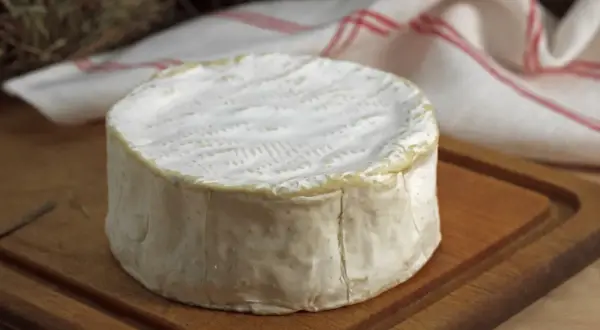 Un delicioso queso francés, con su corteza blanca y cremosa, descansa sobre una tabla de madera.