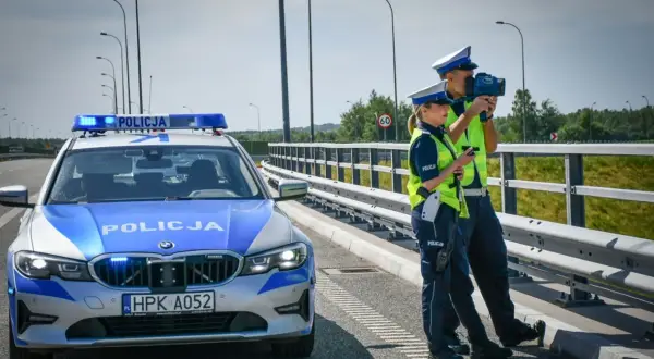 Policjanci kontrolują prędkość na drodze. Obok radiowóz z włączonymi sygnałami. Bezpieczne prowadzenie pojazdu to priorytet.