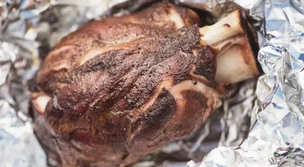 Stinco di maiale succulento, cotto alla perfezione e avvolto in carta stagnola, pronto per essere gustato.