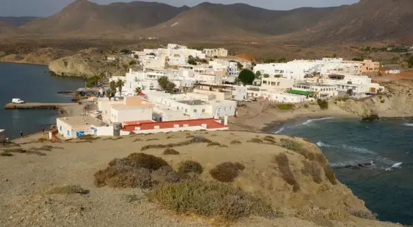 Vista panorámica de la playa Isleta del Moro, con casas blancas, mar azul y montañas áridas al fondo.