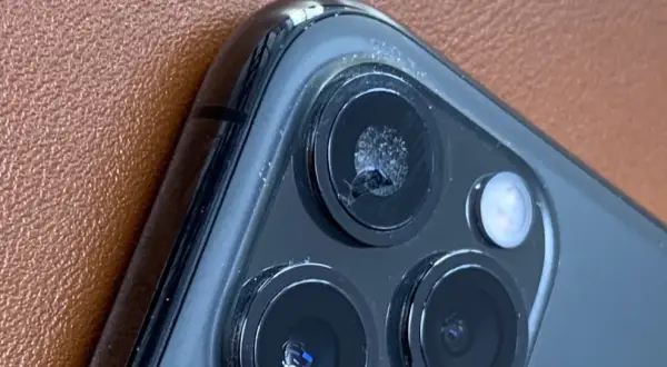 Zbliżenie na pęknięte szkło aparatu iPhone'a na brązowym tle.