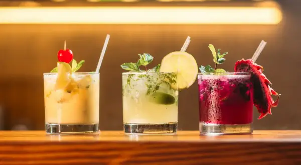Trzy orzeźwiające drinki z wódką: żółty z wiśnią, zielony z limonką i miętą, oraz purpurowy z pitają.