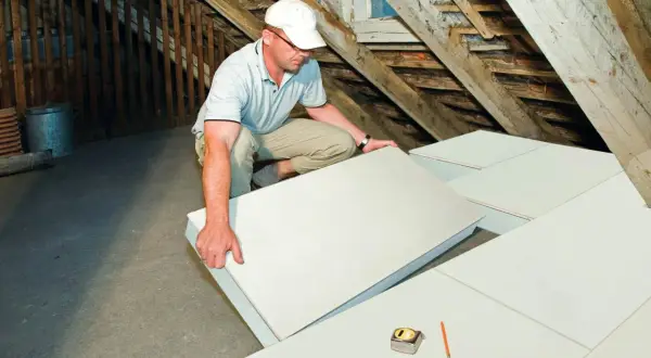 Operaio posa pannelli per isolamento termico in sottotetto. Materiali isolanti edilizia per un tetto efficiente.