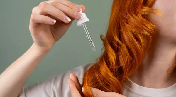 Manos aplicando aceite en cabello pelirrojo. El hair oiling nutre y da brillo.
