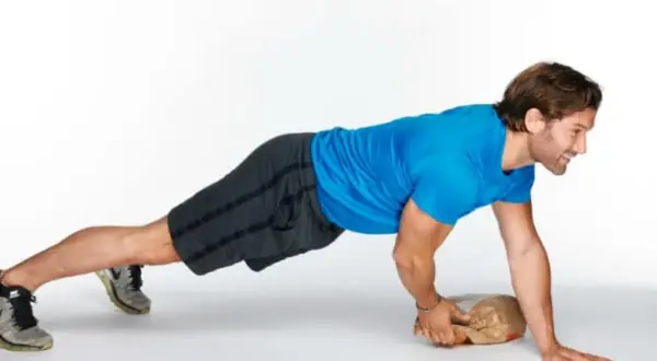Man performing an around the world plank exercise, balancing on one hand and a paper bag.