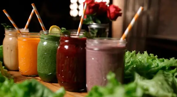 Fem färgglada smoothies i glasburkar, redo för en bebis att njuta av. Grönt, orange, rött och lila.