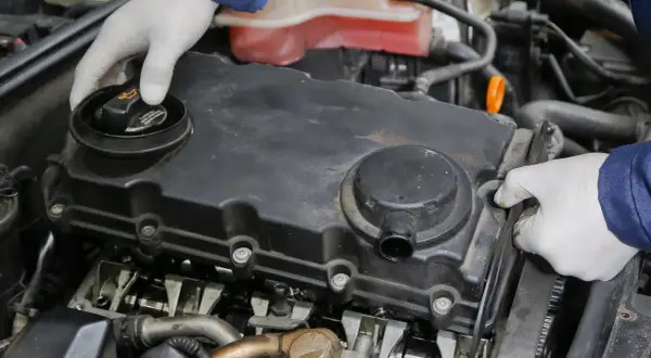 Mechanik w białych rękawiczkach sprawdza silnik, szukając miejsca, gdzie jest odma olejowa.