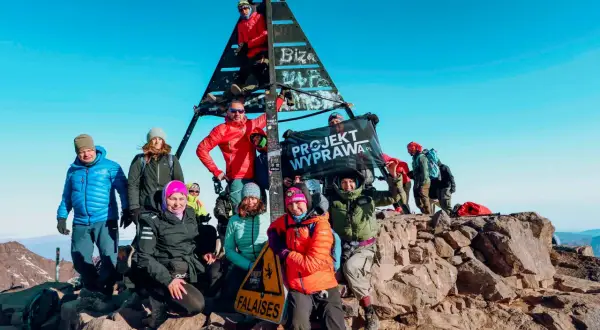 Grupa zdobywców na szczycie Jebel Toubkal podczas trekkingu. Radosna ekipa z flagą "Projekt Wyprawa.pl" cieszy się sukcesem.