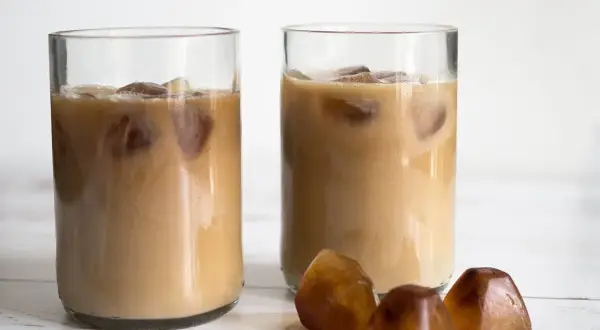 Två glas med iskaffe, perfekt för ett enkelt iskaffe recept. Tre kaffekuber ligger framför.