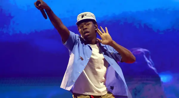 Tyler The Creator w Krakowie, w niebieskiej koszuli i czapce, z mikrofonem w dłoni.