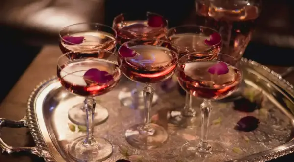 Eleganckie kieliszki z różowym winem, ozdobione płatkami róży, czekają na degustację. W tle widać karafkę z tym samym trunkiem, być może to wykwintny tokaji aszu.