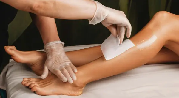 Una mano guantata applica una striscia di cera su una gamba. Per una ceretta efficace, i peli devono essere lunghi circa mezzo centimetro.
