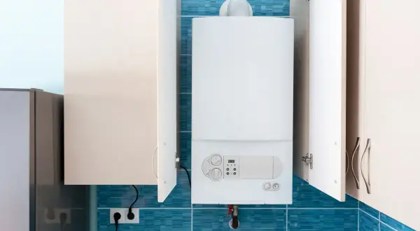 Une chaudière blanche est installée dans un coffrage mural, avec des portes ouvertes révélant le fond carrelé de bleu.