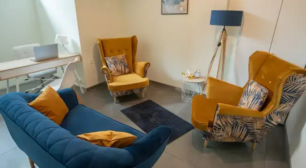 Wnętrze gabinetu psychologicznego z kanapą i fotelami w kolorach niebieskim i żółtym.