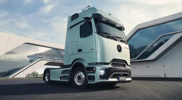 Le dernier camion Mercedes, d'un bleu pâle, est garé devant un bâtiment moderne aux formes courbes et vitrées.