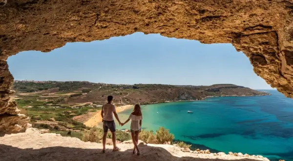 Para zakochanych podziwia widok na turkusowe morze i piaszczystą plażę z jaskini. Malta pogoda w lutym zachwyca słońcem.