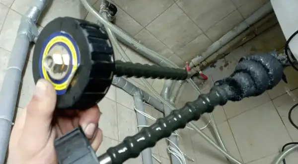 Domowy sposób na czyszczenie instalacji: ręka trzyma narzędzie z okrągłą głowicą, podłączone do elastycznego węża, który prowadzi do rur.