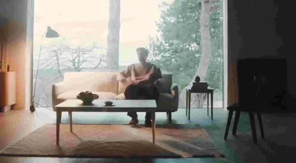 En person sitter i en soffa i ett rum med dansk design inredning. Ett stort fönster visar en vinterskog.