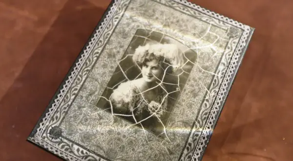 Stare zdjęcie kobiety z fryzurą w stylu retro, pęknięte i umieszczone na ozdobnej powierzchni.