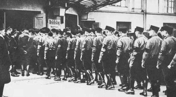 Männer in Uniformen marschieren vor dem Reichstag. Die Szene erinnert an die Zeit der deutschen Zentrumspartei, als politische Organisationen eine wichtige Rolle spielten.