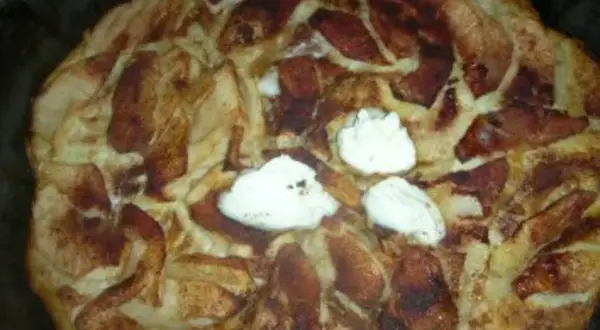 Ein frisch gebackener Apfel-Scheiterhaufen mit Zimt und drei Klecksen Sahne. Ein köstliches Rezept für gemütliche Stunden.