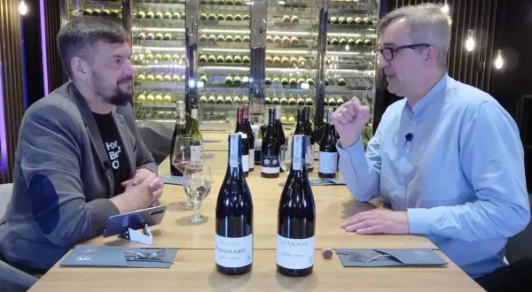 Dwóch mężczyzn przy stole degustuje wino. Na stole stoją butelki, w tym dwie z etykietami sugerującymi pinot noir.